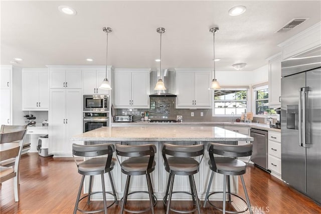 kitchen featuring built in appliances, dark wood-style flooring, visible vents, white cabinetry, and wall chimney range hood
