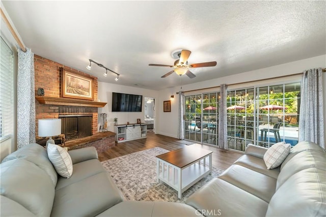living area featuring wood finished floors, rail lighting, a fireplace, ceiling fan, and baseboards
