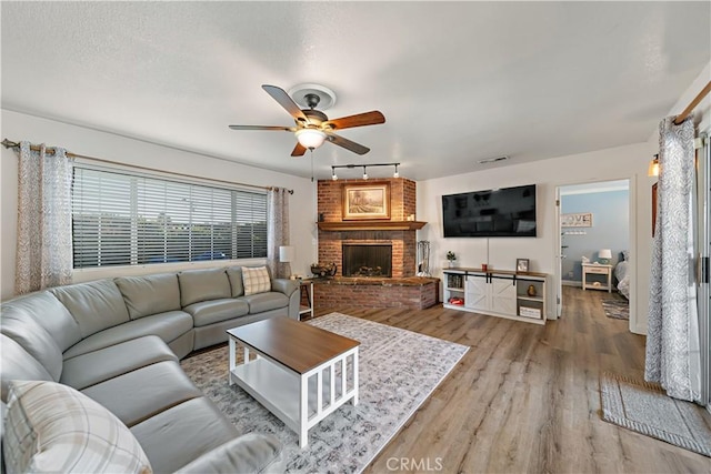 living room with ceiling fan, a brick fireplace, rail lighting, and wood finished floors