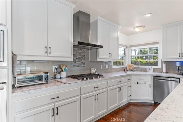 kitchen with wall chimney range hood, white cabinetry, stainless steel appliances, and a sink