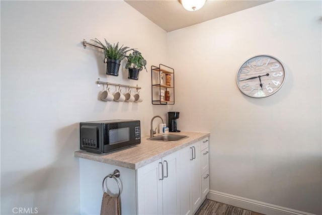 bar with baseboards, black microwave, and a sink