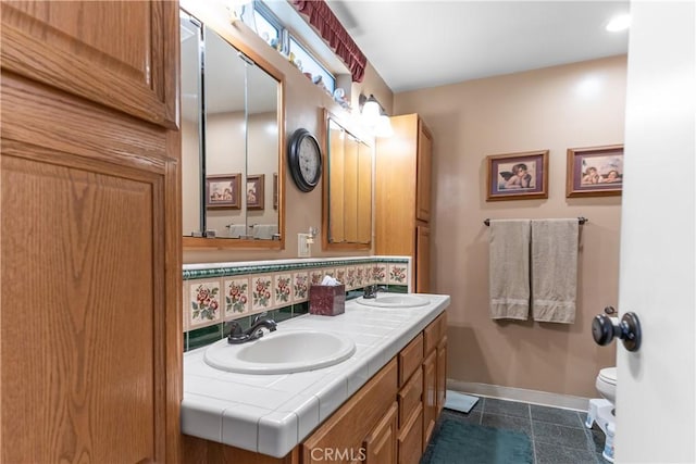 bathroom with double vanity, toilet, baseboards, and a sink