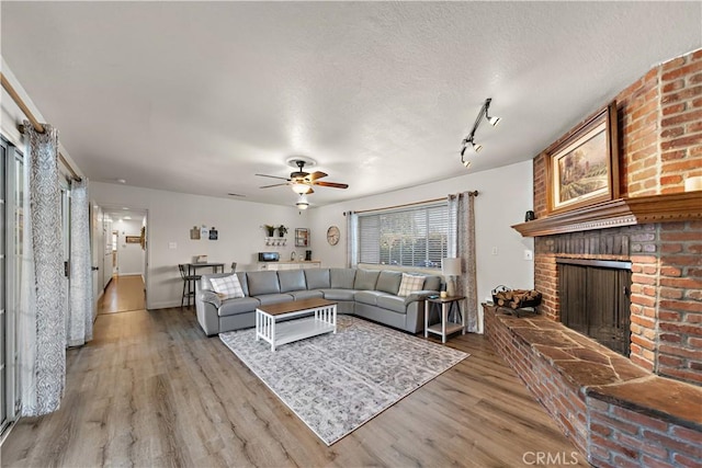 living area with a textured ceiling, light wood-type flooring, a brick fireplace, a ceiling fan, and baseboards