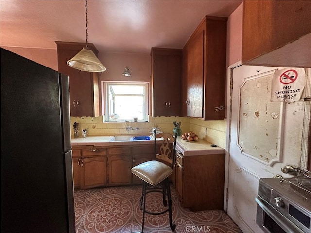 606 W 57th St, Los Angeles, CA 90037 - kitchen with freestanding refrigerator, tile countertops, a sink, backsplash, and brown cabinetry
