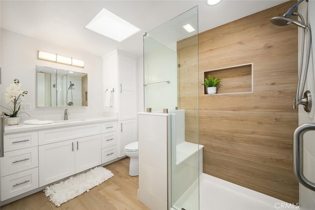 full bath featuring toilet, a skylight, wood finished floors, vanity, and a shower stall