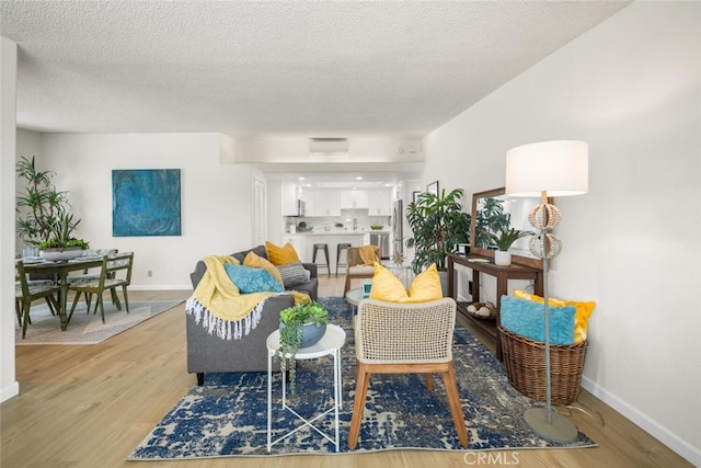 living area featuring light wood finished floors, a textured ceiling, and baseboards
