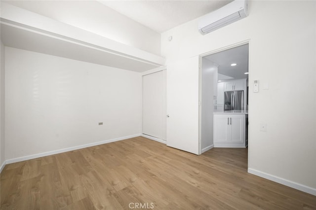 unfurnished room with a wall mounted air conditioner, light wood-style flooring, and baseboards