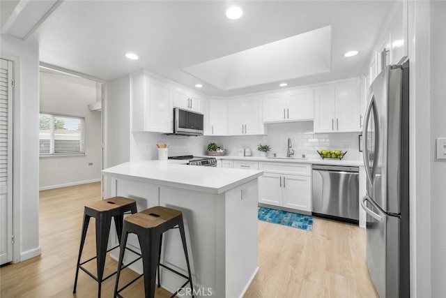 kitchen featuring a breakfast bar, light wood finished floors, a sink, white cabinetry, and appliances with stainless steel finishes