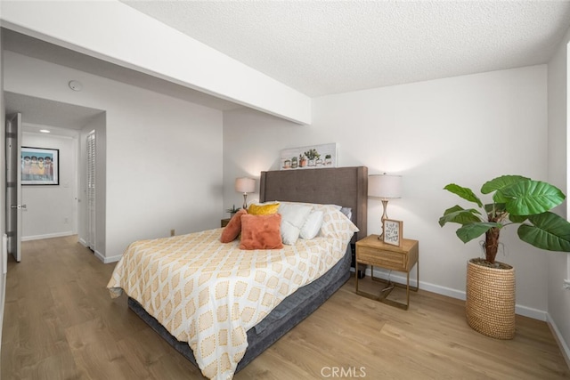 bedroom featuring a textured ceiling, baseboards, and wood finished floors