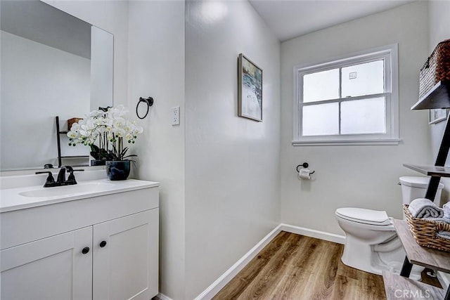 half bath with vanity, toilet, baseboards, and wood finished floors
