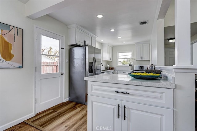 kitchen with light wood-style flooring, recessed lighting, light stone counters, white cabinetry, and stainless steel fridge