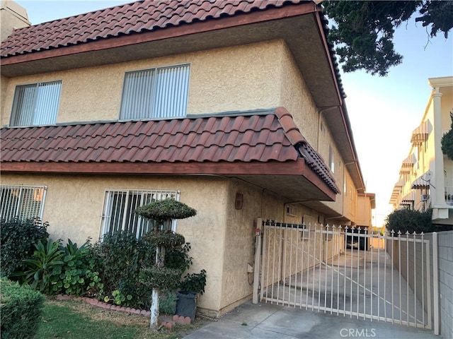 view of home's exterior with stucco siding, a tile roof, fence, and a gate
