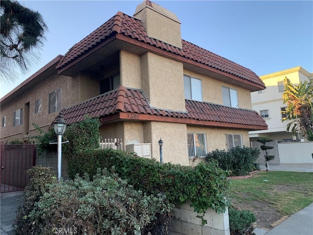 view of home's exterior with stucco siding, fence, and a tiled roof