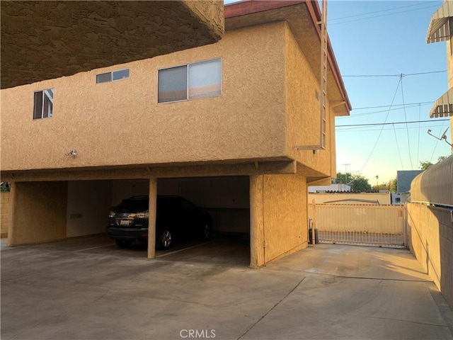 view of side of home with a gate, fence, an attached garage, and stucco siding