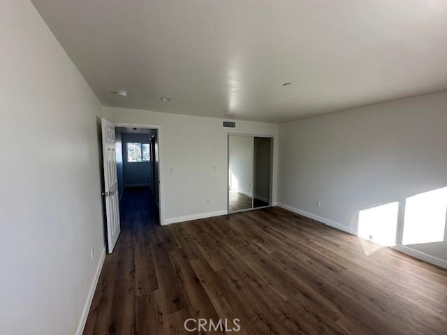 5507 S Manhattan Pl, Los Angeles, CA 90062 - unfurnished bedroom with baseboards, dark wood-type flooring, and a closet