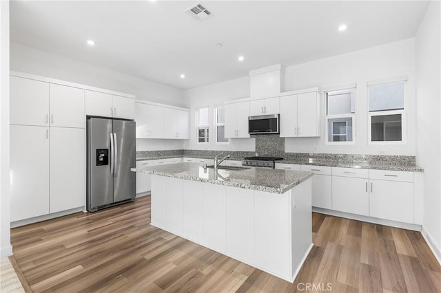 kitchen with visible vents, a sink, wood finished floors, a center island with sink, and stainless steel appliances
