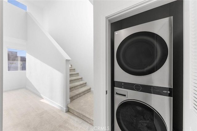 laundry area with baseboards, stacked washer and dryer, laundry area, and carpet