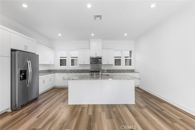 kitchen with a sink, stainless steel appliances, a kitchen island with sink, white cabinetry, and light wood-style floors