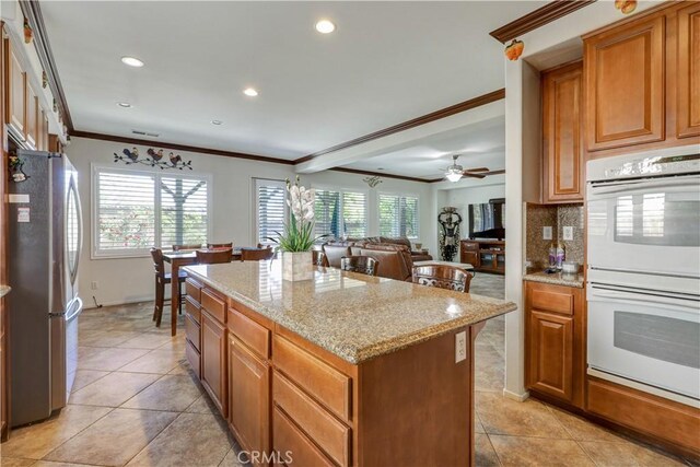31710 Waterfall Way, Murrieta, CA 92563 - kitchen featuring a center island, freestanding refrigerator, white double oven, light stone counters, and ornamental molding