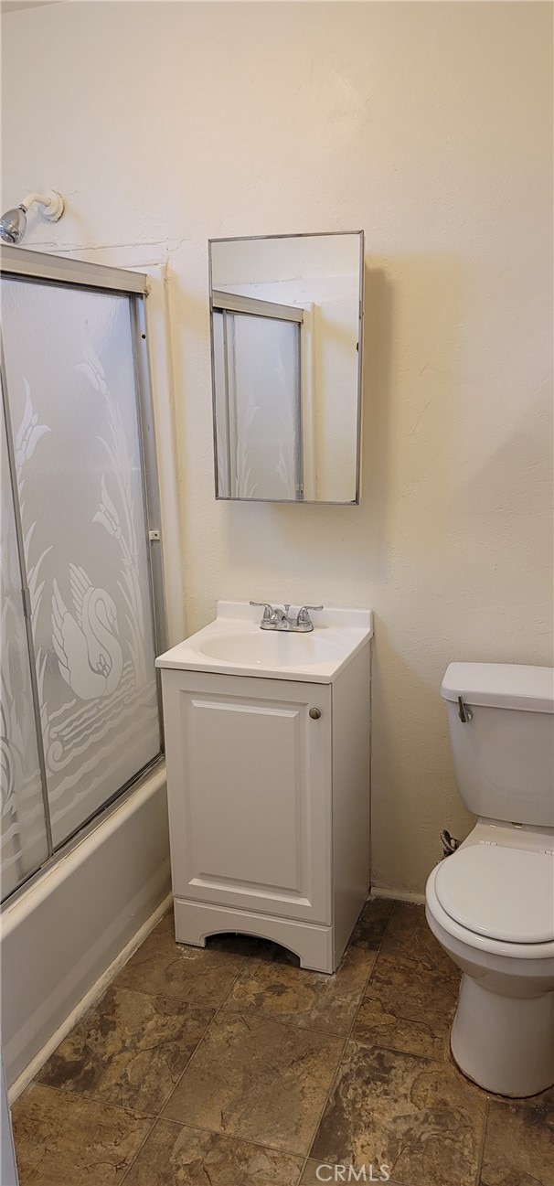 954 N Van Ness Ave, Los Angeles, CA 90038 - bathroom featuring toilet, vanity, stone finish floor, bath / shower combo with glass door, and baseboards