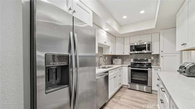 kitchen featuring appliances with stainless steel finishes, a sink, white cabinetry, light wood finished floors, and tasteful backsplash