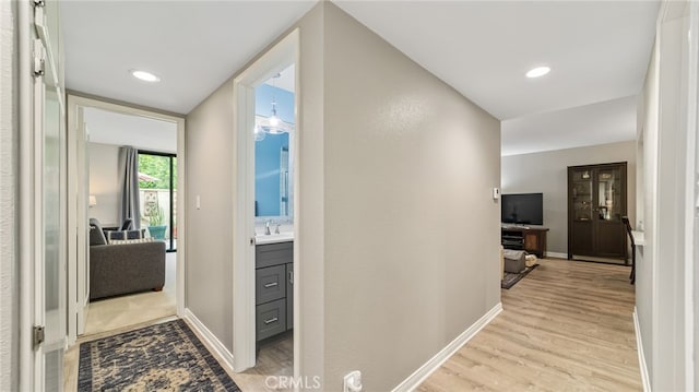 hall featuring light wood-style floors, baseboards, a sink, and recessed lighting