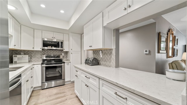 kitchen with stainless steel appliances, white cabinetry, light wood finished floors, recessed lighting, and tasteful backsplash