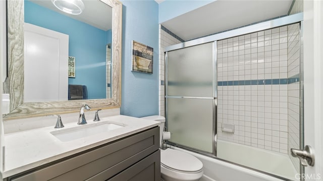 full bath with toilet, vanity, shower / bath combination with glass door, and a textured wall