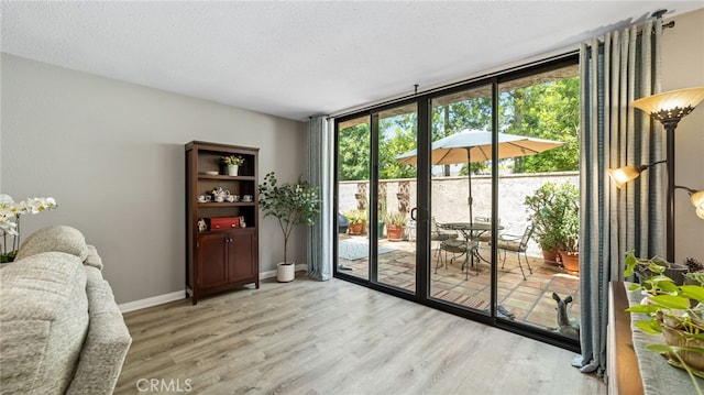 doorway with light wood-style floors, a textured ceiling, and baseboards