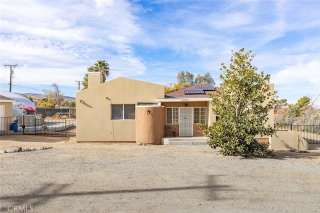 southwest-style home with roof mounted solar panels, stucco siding, and fence