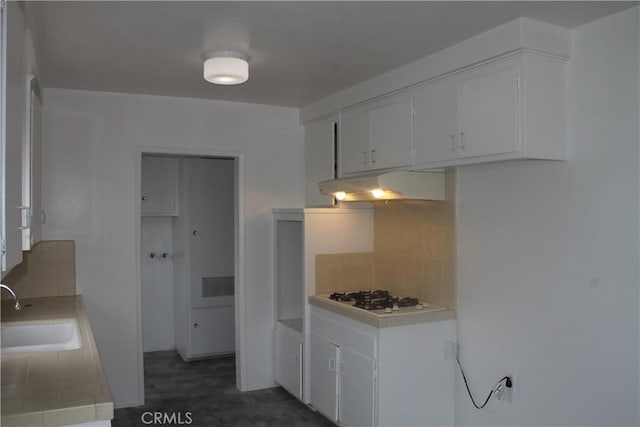 kitchen featuring a sink, white gas cooktop, under cabinet range hood, backsplash, and light countertops