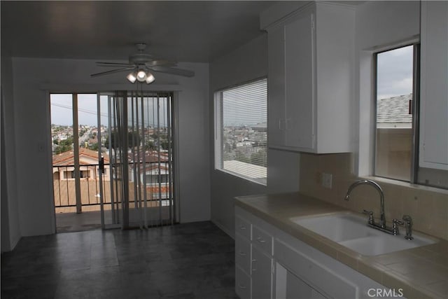 kitchen featuring a ceiling fan, a sink, tile counters, a wealth of natural light, and decorative backsplash