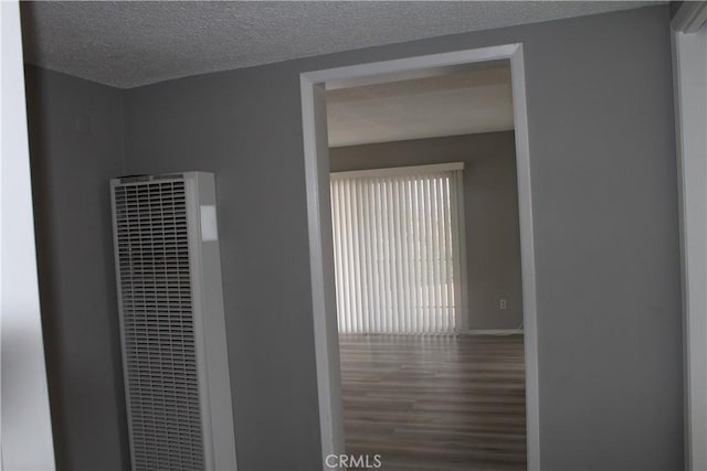 corridor featuring baseboards, a heating unit, a textured ceiling, and wood finished floors