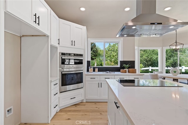 44240 La Cruz Dr, Temecula, CA 92590 - kitchen with black electric stovetop, stainless steel double oven, ventilation hood, light wood finished floors, and white cabinets