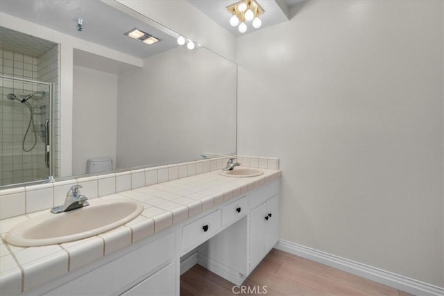 full bathroom featuring double vanity, wood finished floors, a stall shower, and a sink
