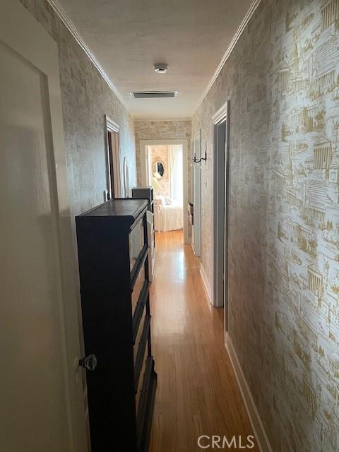 corridor featuring crown molding, visible vents, wood finished floors, and baseboards