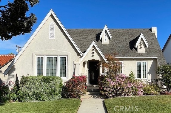 english style home with stucco siding, roof with shingles, and a front yard