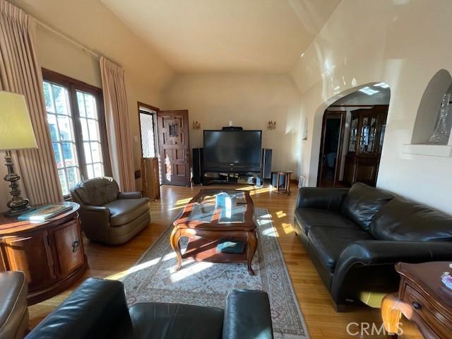 living area featuring arched walkways, wood finished floors, and vaulted ceiling