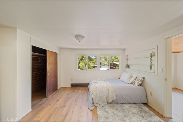 bedroom with light wood finished floors, a closet, and a baseboard radiator