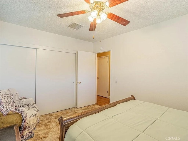 carpeted bedroom featuring a closet, a textured ceiling, visible vents, and a ceiling fan