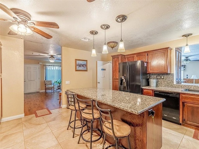 kitchen featuring brown cabinetry, a textured ceiling, ceiling fan, black appliances, and a kitchen island