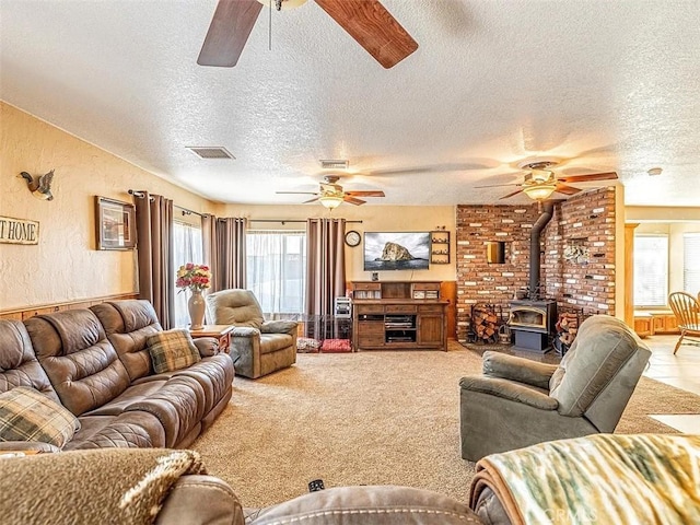 living room featuring a wood stove, a textured ceiling, visible vents, and ceiling fan