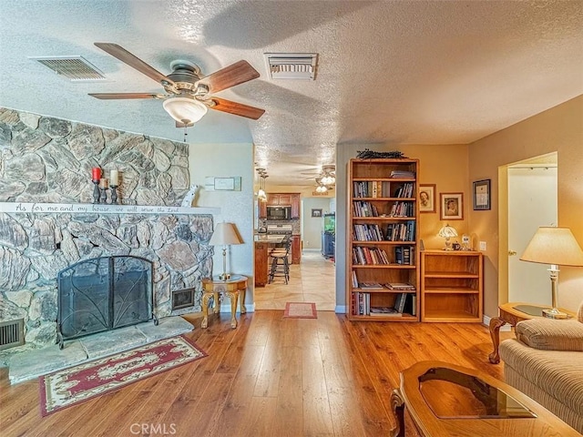 living room featuring a textured ceiling, visible vents, wood-type flooring, and ceiling fan
