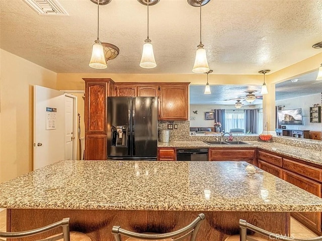 kitchen featuring a textured ceiling, visible vents, a sink, a kitchen breakfast bar, and black appliances