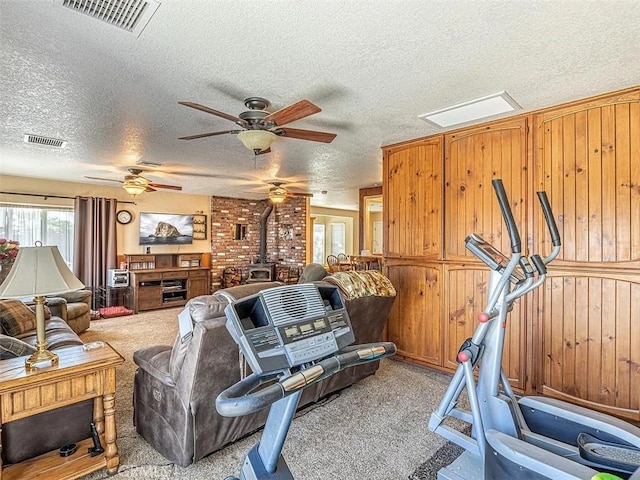 exercise area featuring light carpet, a wood stove, visible vents, and a textured ceiling