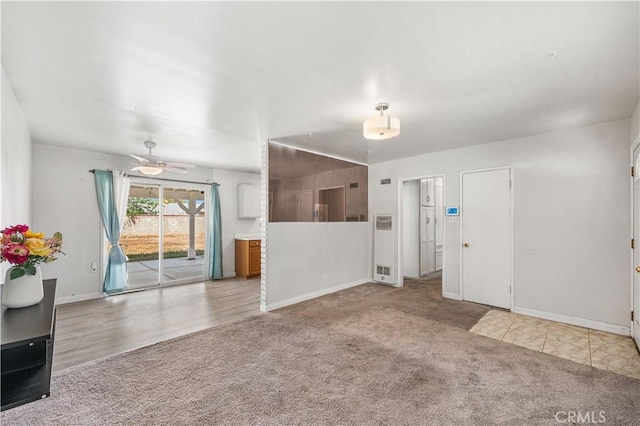 unfurnished living room featuring a heating unit, carpet, baseboards, and a ceiling fan