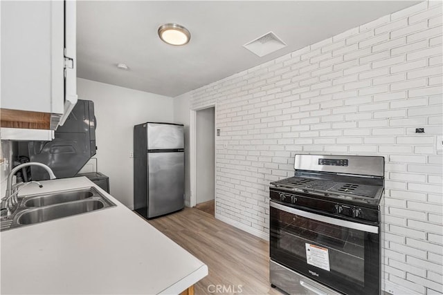 kitchen featuring brick wall, a sink, light wood-style floors, light countertops, and appliances with stainless steel finishes