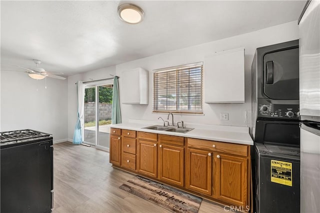 kitchen with a sink, stacked washer and dryer, light countertops, a ceiling fan, and gas range