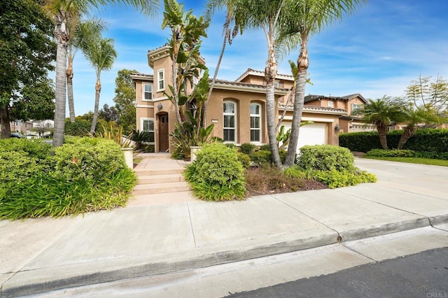mediterranean / spanish-style home featuring concrete driveway, a tiled roof, stucco siding, and a garage
