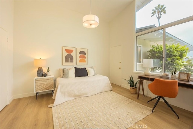 bedroom featuring baseboards, light wood-type flooring, and a high ceiling
